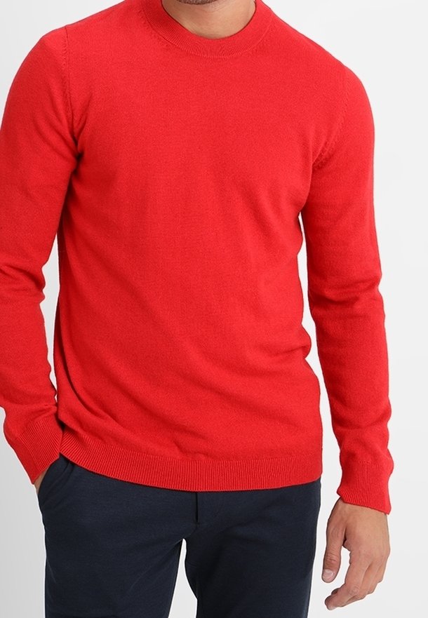 Pull rouge à manches longues avec un col rond, fabriqué en tissu doux, avec des poignets et un ourlet côtelés, porté avec un pantalon foncé.