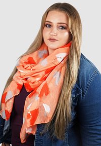 Felle oranje sjaal met rode en grijze abstracte bladmotieven, lichte stof, om de nek gedrapeerd, gelaagd en iets textuur.