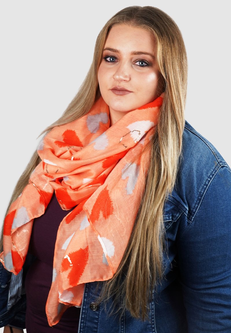 Felle oranje sjaal met rode en grijze abstracte bladmotieven, lichte stof, om de nek gedrapeerd, gelaagd en iets textuur.