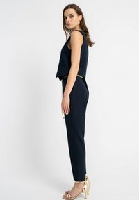 Granatowy top bez rękawów o kroju cropped, połączony z dopasowanymi granatowymi spodniami i złotymi akcentami, w tym łańcuszkowym paskiem i sandałami na obcasie.