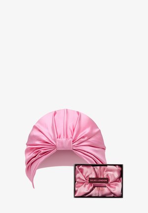 Rosa satinierte Haarband mit einem großen, verdrehten Knoten-Detail, präsentiert über einer passenden satinierte Aufbewahrungsbox, die ein Logo an der Seite trägt.