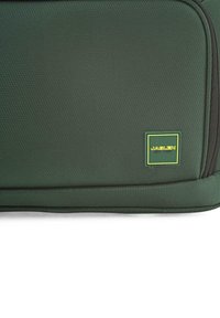 Material de mochila texturizado en verde con forma rectangular, que presenta un acento de logo amarillo y verde y un cierre de cremallera resistente.