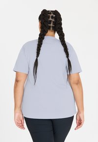 Lys grå kortærmet t-shirt med rund halsudskæring, glat tekstur, let løs pasform, båret med sorte leggings, set fra ryggen.