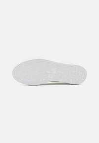Weiße Sneaker-Sohle mit strukturiertem Gummi für Halt, ausgestattet mit einem dezenten Markenlogo und einem geschwungenen Design für Komfort und Unterstützung.