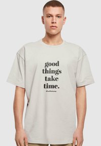 Hele hall vasakate varrukatega heledat halli t-särki, mis on valmistatud puuvillast ja millel on must tekst "head asjad võtavad aega." Lisatud hashtag #TrustTheJourney.