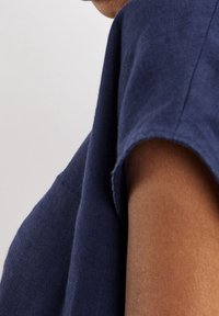 Vêtement en lin bleu marine avec un col rond et des manches courtes, présentant une texture lisse et une coupe décontractée, mettant en avant la simplicité du design.