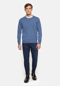 Blauer Rundhals-Pullover aus Strickstoff, kombiniert mit dunkelblauen Jeans und schwarzen Stiefeletten. Mit gerippten Bündchen und Saum. Kleines Logodesign.