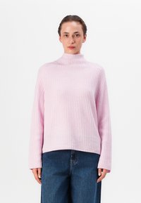 Pulover din tricot de culoare roz deschis, cu guler înalt și mâneci lungi, având o croială relaxată, asortat cu blugi largi de culoare albastru închis.