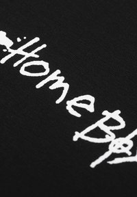 Svart tekstil med hvit håndskrevet tekst som sier "HomeBoy." Stoffet har en jevn og glatt tekstur.