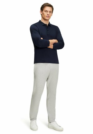 Navyblaues Langarm-Polohemd kombiniert mit hellgrauen Jogginghosen und weißen Turnschuhen. Der Stoff wirkt glatt; das Hemd hat eine Drei-Knopf-Leiste.