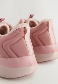 Scarpe da ginnastica rosa con una parte superiore in tessuto testurizzato, collo imbottito e suola ammortizzata. Presentano un tallone rinforzato e un passante per il tallone.