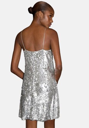 Vestido plateado de lentejuelas con un corte holgado, tirantes finos y espalda con escote en forma de U. La tela tiene una superficie texturizada y reflectante.