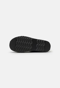 Suela de zapato negra con un patrón de tracción en zigzag, hecha de goma, con superficie texturizada y ligero desgaste.