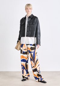 Black leather cropped jacket with two front pockets, white button-up shirt, and patterned wide-leg trousers in orange, blue, and brown tones.