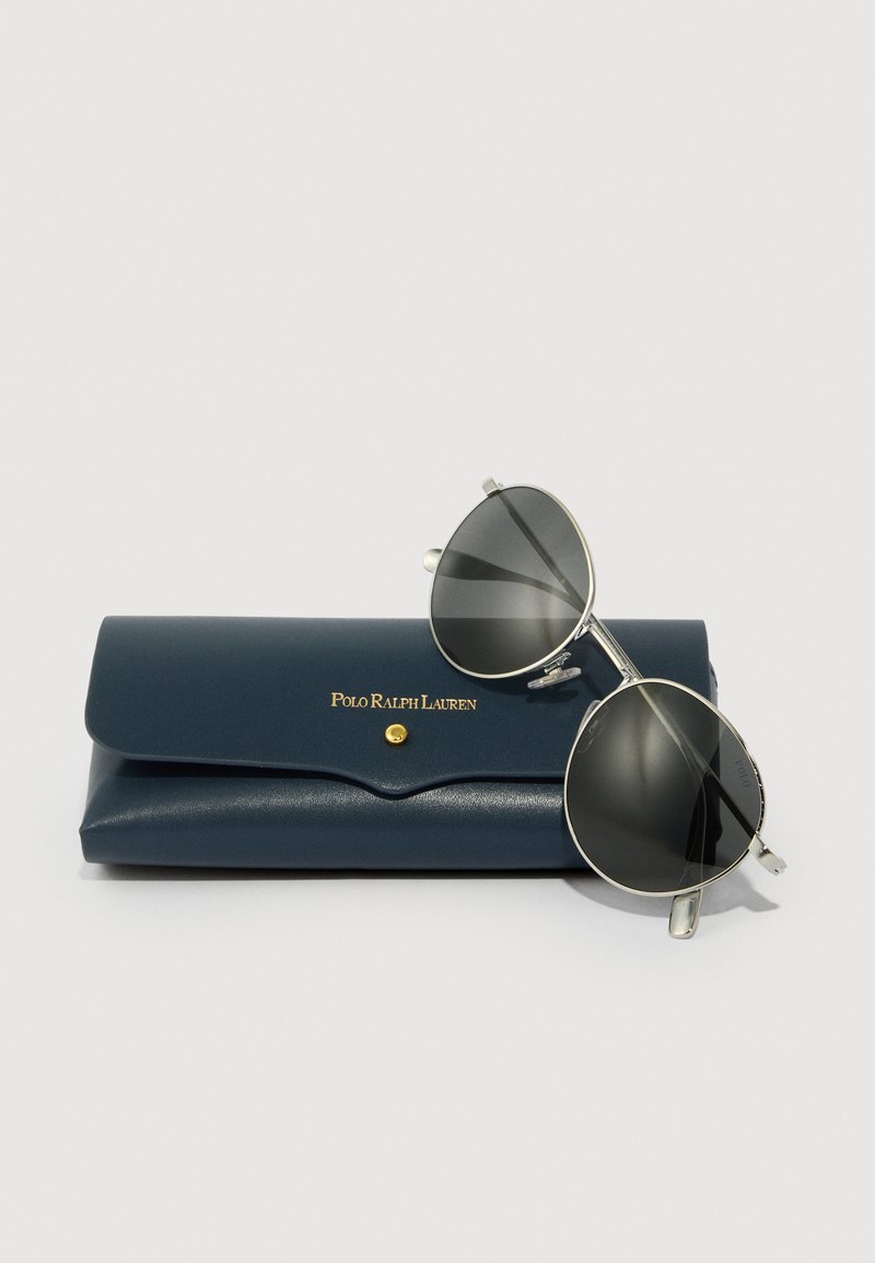 Silver aviator sunglasses with dark lenses, resting on a navy blue leather case featuring a gold logo and a snap closure.