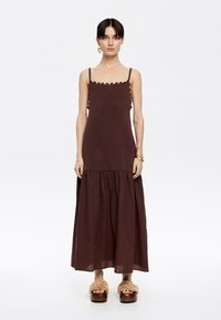 Abito midi senza maniche marrone con scollatura scallop, design a strati e texture morbida. Abbinato a calzature voluminosi con dettagli floreali.