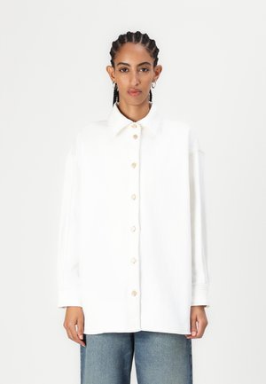 Hvit oversized skjorte med knapper laget av bomull, med klassisk krage, i tillegg til treknapper og senkede skuldre, kombinert med blå denim.