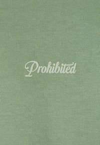 Tissu texturé vert arborant le mot "Interdit" en lettres cursives blanches, positionné au centre.