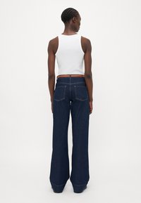 Široke temne jeans hlače z visokim pasom, zapenjanjem na gumb in dvema zadnjima žepoma. Ujemajoče se z ozkim belim topom brez rokavov.