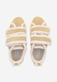 Beige mokkasiner i semsket skinn med hvite, fluffy stropper og fòr. Tykk såle, rund tå-design, og en etikett synlig inni.