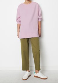 Sudadera de gran tamaño en color rosa claro con escote redondo, combinada con pantalones de pernera ajustada en color verde oliva. Estilizada con zapatillas deportivas blancas y suelas de goma.