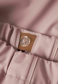 Lys rosa vanntett stoff med en bred rynket midje og en brun tekstilaccent med en gjennomsiktig knappedetalj.