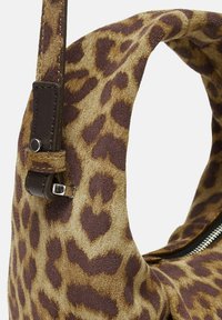 Sac en imitation léopard avec un matériau en daim marron, une poignée courbée et des accents en métal près de la sangle. Surface texturée avec un motif proéminent.
