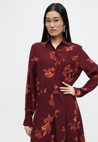 Μπλουζάκι μπορντώ με κουμπιά, με floral κέντημα σε πορτοκαλί και ροζ, μακριά μανίκια και κωνικό γιακά με μπροστινή τσέπη.