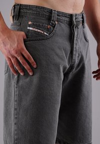 Close-up of a person wearing gray denim shorts with a visible small front pocket and their left hand resting on the thigh.