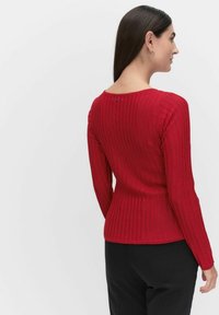 Rode geribbelde trui met lange mouwen, voorzien van een fitted ontwerp en een klein knoopdetail op de achterkant van de nek. Zachte textuur, minimaal patroon.