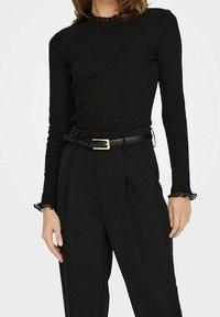 Svart långärmad topp med rynkad halsringning, kombinerad med högmidjade svarta byxor och ett svart bälte med detalj av ett guldspänne.