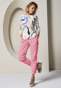 Meer gekleurde trui met abstracte wervelingen in roze, blauw, groen en marineblauw; gecombineerd met roze broek en bruine sleehakken.