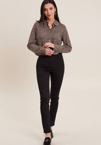 Chemise à boutons en imprimé léopard, fabriquée en tissu doux, associée à un pantalon noir ajusté. La tenue se distingue par son col classique et ses accents élégants.