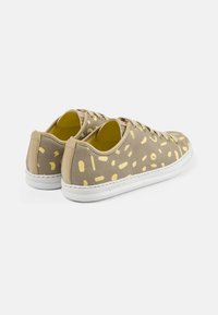 Beige sneakers med ett texturerat tyg som har gula abstrakta mönster, vit gummisula och ljusbruna detaljer på hälen.