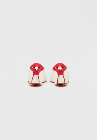 Hvite sko med røde gummidetaljer og maljer. Har en klaff for enkel påsetting og en teksturert brun såle for grep.