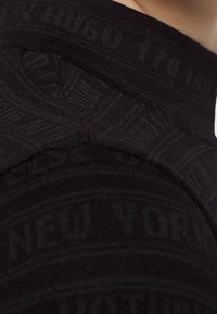 Vêtement noir présentant un tricot texturé avec un motif subtil "New York" et une coupe ajustée. Le col est côtelé, ajoutant du détail à l'ensemble.