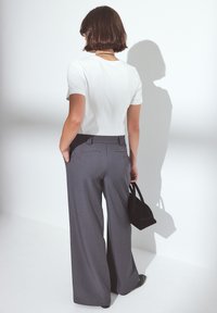 Harmaat leveät housut korkealla vyötäröllä, yhdistetty valkoiseen istuvaan yläosaan. Pienempi musta käsilaukku pidetään kädessä.