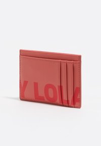 Tarjetero de cuero coral con textura de grano sutil, que cuenta con cuatro ranuras para tarjetas y un logo impreso en negrita en la parte frontal.