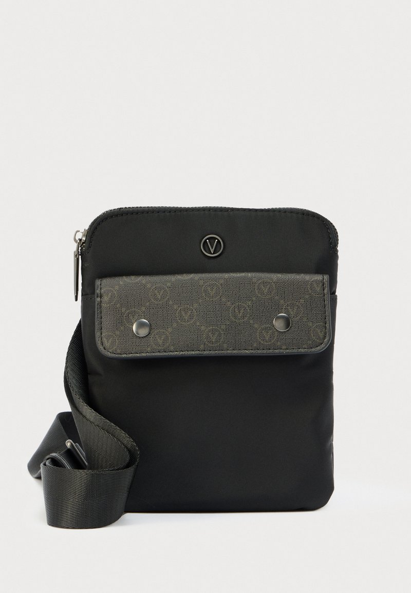 Majhna črna torbica čez ramo z nastavljivim trakom, siva sprednja preklopna z vzorcem in kovinskimi gumbi na pritrditev ter z zgornjo zadrgo.