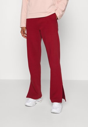 Personne portant un pantalon large rouge avec des fentes latérales et des baskets blanches, associé à un haut à manches longues rose clair.