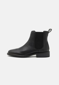 Botín Chelsea de cuero negro con panel lateral elástico, punta redondeada y tacón bajo apilado. Presenta una lengüeta para facilitar su uso.