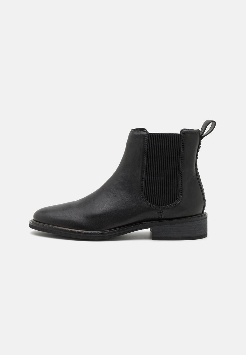 Botín Chelsea de cuero negro con panel lateral elástico, punta redondeada y tacón bajo apilado. Presenta una lengüeta para facilitar su uso.