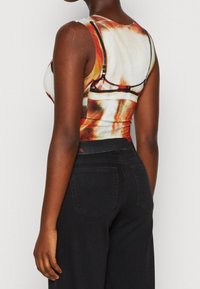 Dopasowany bezrękawnik z wielokolorowym abstrakcyjnym wzorem, wykonany z elastycznej tkaniny. Noszony z czarnymi jeansami o wysokim stanie.