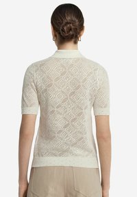 Stickad polo t-shirt i ljusbeige med ett texturerat, öppet mönster. Korta ärmar och ribbad krage. Diskret detaljering längs nederkanten.