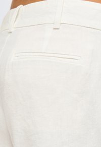 Κοντινή λήψη από το πίσω μέρος λευκού παντελονιού με μία οριζόντια τσέπη και θηλιές για ζώνη στη μέση.