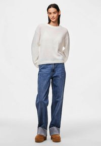 White, textured sweater with drop shoulders; paired with loose blue denim jeans, featuring a frayed hem and tan suede platform shoes.