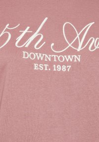 Vaaleanpunainen kangaspaita, jossa on valkoista brodeerattua tekstiä, joka lukee "5th Ave DOWNTOWN EST. 1987." Sileä pinta, lyhyet hihat, rento malli.