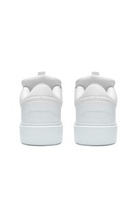 Valkoiset tennarit, joissa on sileä nahkainen yläosa, pehmustettu kaulus ja kumipohja. Vähäinen brändäys ja takana vetotappi.