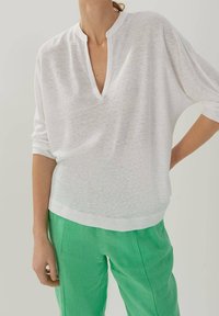 Vit lättviktig topp med V-ringning och trekvartsärmar, i kombination med gröna linbyxor. Mjuk textur, avslappnad design.