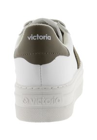 Sneaker bianca con un tab del tallone texturizzato beige. Presenta una suola spessa e bianca e un design cucito, con il nome del marchio inciso sul tallone.